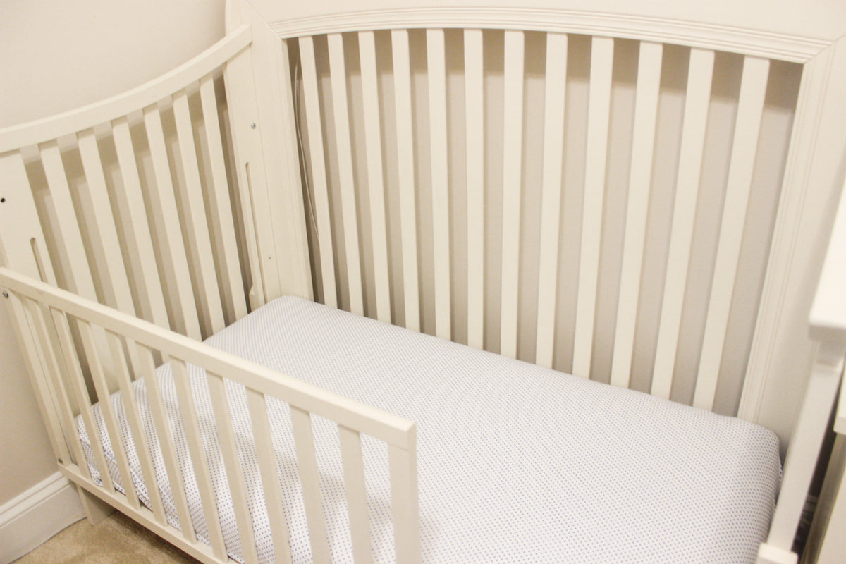 Crib with white crib sheet with navy blue polka dots.